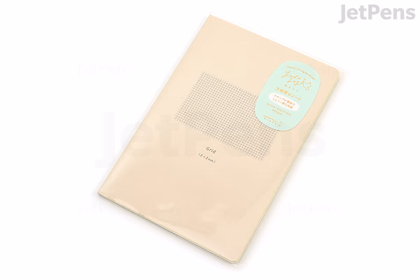 A beige Midori Yuru Log Notebook in B6 size with MD Thick paper and 2 mm grid pattern, shown in its clear plastic packaging with a light blue label.