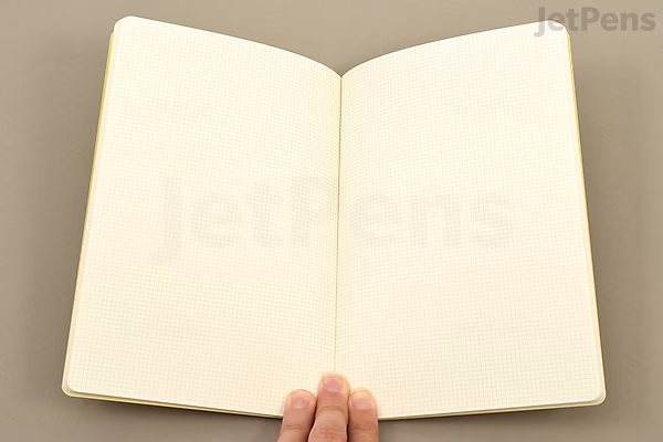 Open Midori Yuru Log Notebook in B6 size with beige, thick 2 mm grid pages, held by a hand at the bottom center.