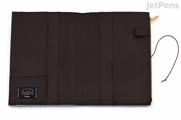 Beige cloth notebook cover for B6 size, featuring multiple vertical pockets and a small strap closure on the right side. A black label with white text is sewn on the bottom left corner.