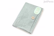 Light blue cloth notebook cover with a zipper, designed for B6-sized notebooks, featuring a small round wooden button and a white oval label on the front.