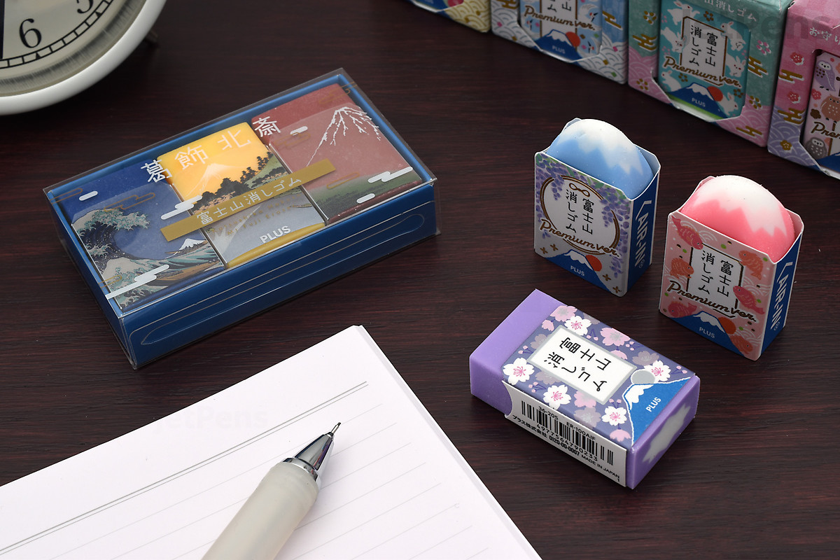 Mt. Fuji Eraser picture that depicts three erasers, a notebook and a box with erasers. a few erasers have been used enough to show the forming of the Mt. Fuji shape and color.
