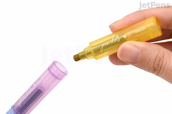 A hand holding a yellow Midori Join Dots Connecting Marker with its cap removed, positioned near a purple marker cap on a white background. The marker is part of a 3-color bright set.