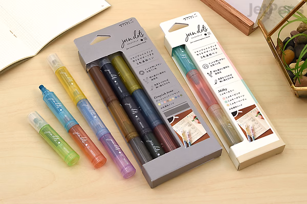 Three Midori Join Dots Connecting Markers in bright green, orange, and blue colors are displayed on a wooden surface next to their packaging boxes. The markers are designed for creating dotted lines and come in a set of three colors.