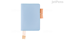 Powder-blue A6 Hobonichi Techo planner with matching cover, peach pen loop and elastic, two peach ribbon bookmarks with gold tassel charms, closed, front view.