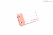 A small A7 pink KOKUYO Campus two-ring binder notebook, open to show lined white pages and a pale pink cover with "Campus" text.